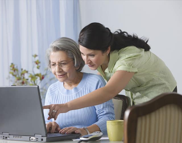 helping_laptop Una mujer joven asiste a una mujer mayor con la computadora portátil