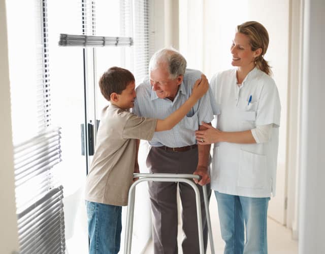 palliative_2 Caregiver Smiles as Young Boy Hugs Elderly Patient