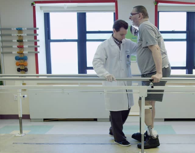 rehab_2 Un fisioterapeuta o médico ayuda a caminar a un hombre con piernas ortopédicas