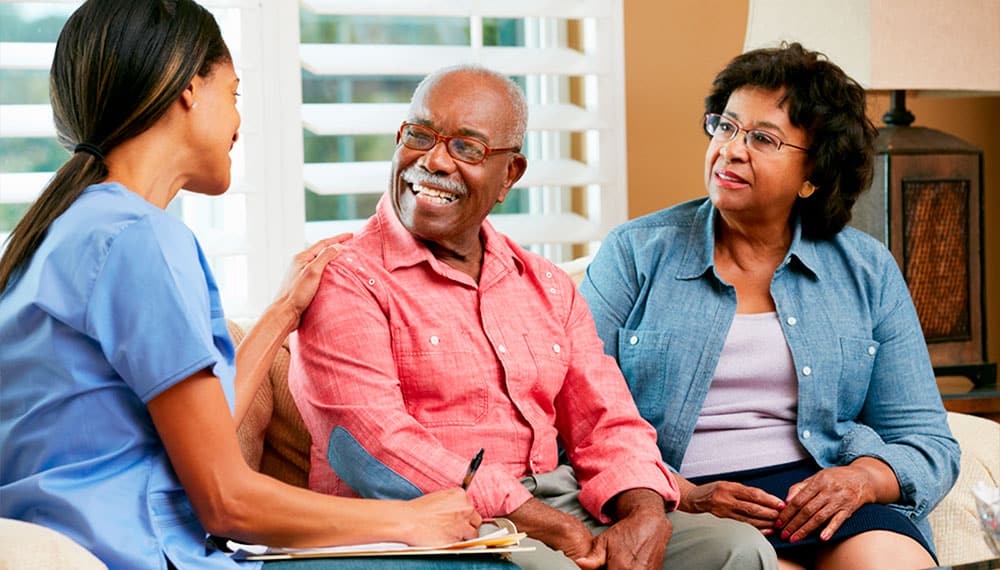 Nurse in Jeans Taking Notes During Home Visit with Middle Aged Couple