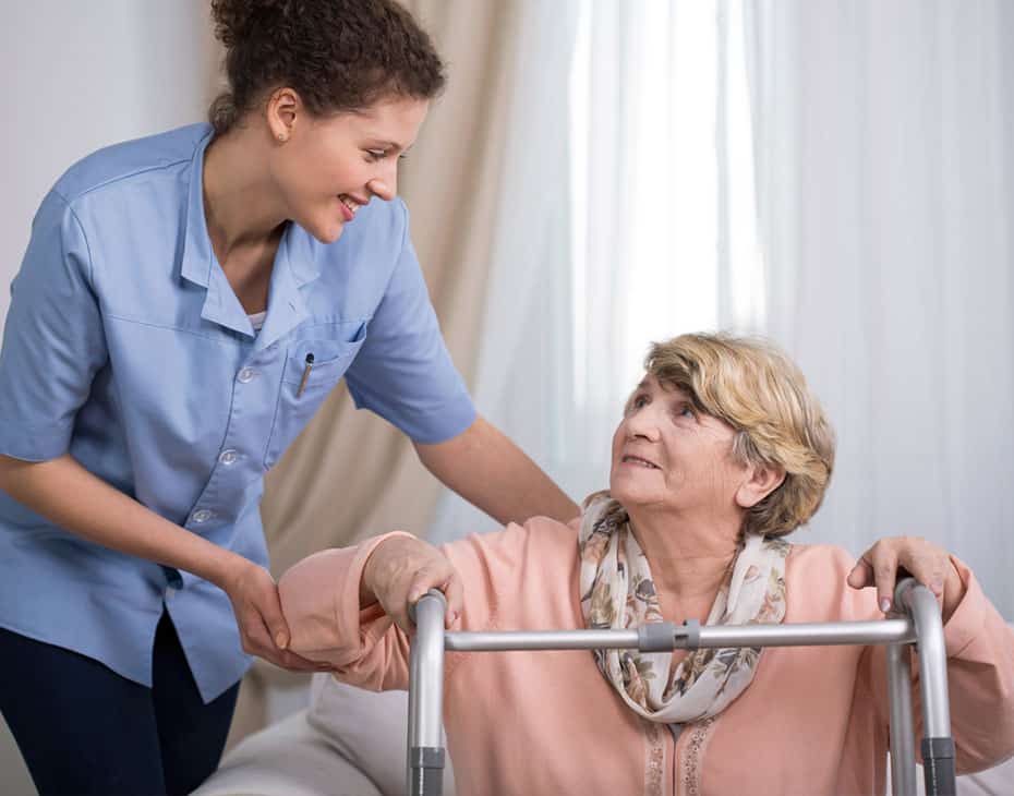 Una cuidadora de MJHS ayuda contenta a una paciente mayor con el andador