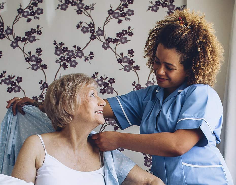 interior_advanced_illness_930x730 Female Home Caregiver Dressing Female Senior in Bedroom