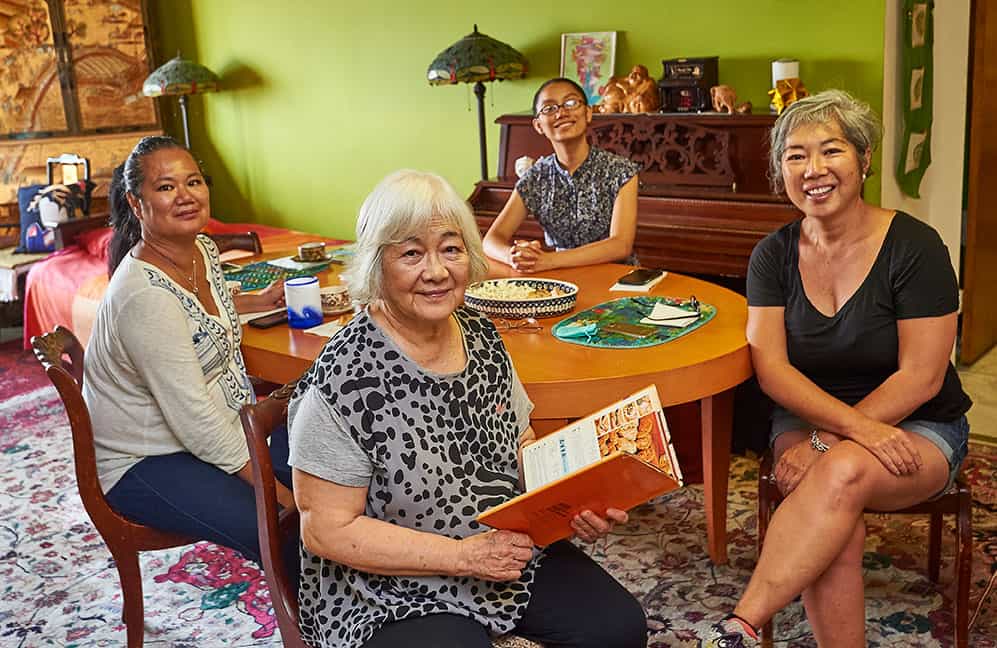 Four Women Sitting Around a Table Look at a Cookbook