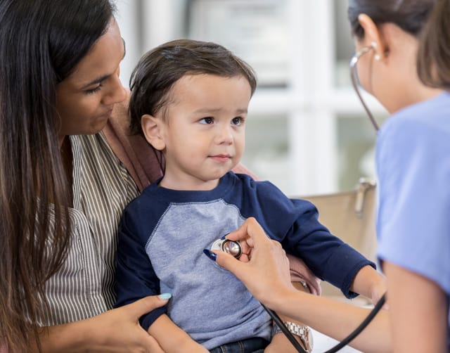 iStock-1056360004-640x502 A young child is held by its mother while a care provider listens to the child's heart with a stethoscope